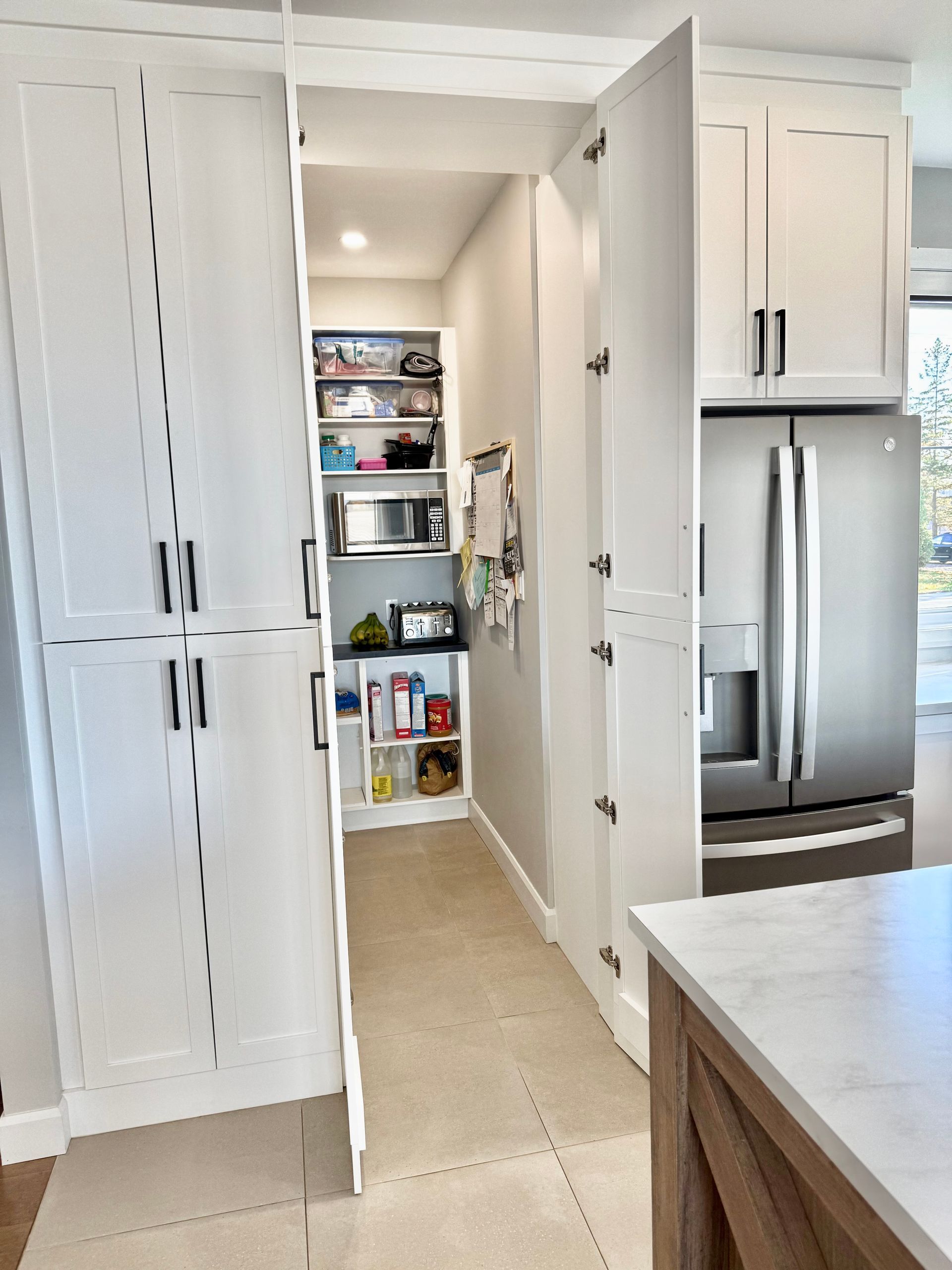 Garde-manger blanc dissimulé derrière des portes d'armoires. Réfrigérateur en acier inoxydable visible.