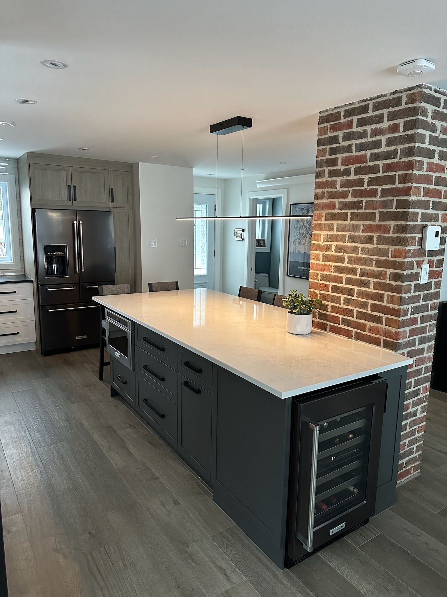 Cuisine moderne avec îlot gris foncé, plan de travail blanc et cave à vin intégrée ; accent de briques apparentes.