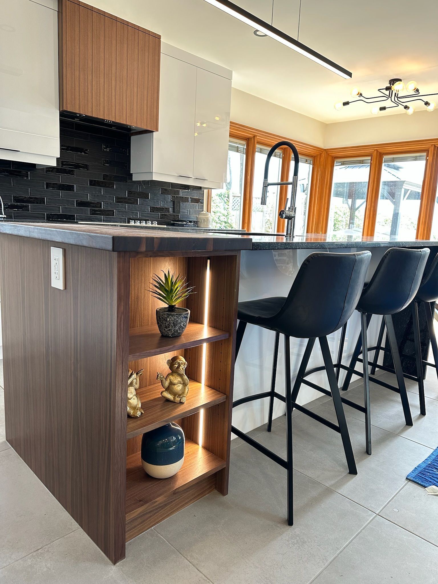 Îlot de cuisine avec étagères ouvertes et tabourets de bar, agrémenté d'objets décoratifs et d'un éclairage intégré.