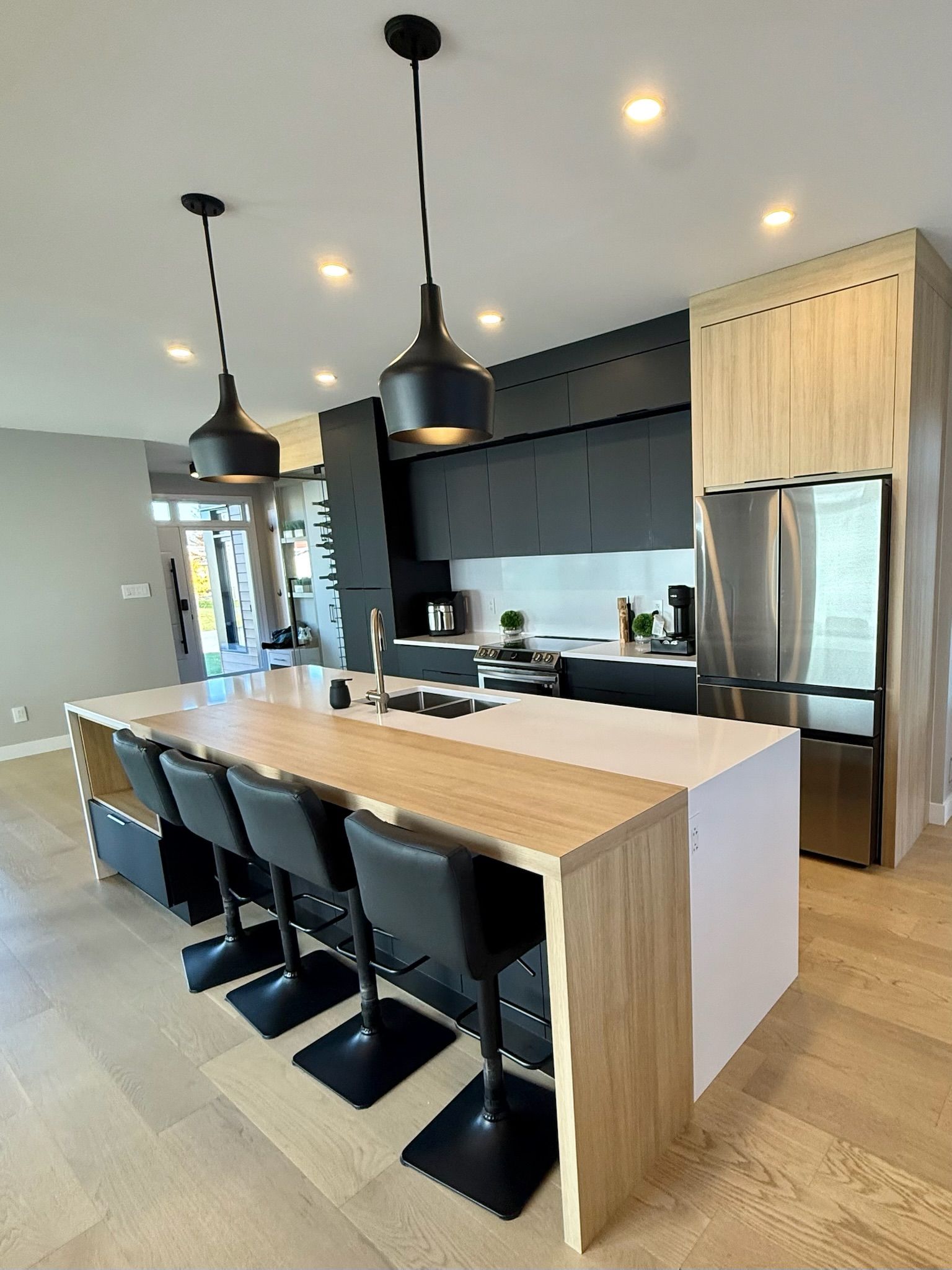 Cuisine moderne avec un grand îlot central, des armoires noires, des appareils électroménagers en acier inoxydable et des éléments en bois.