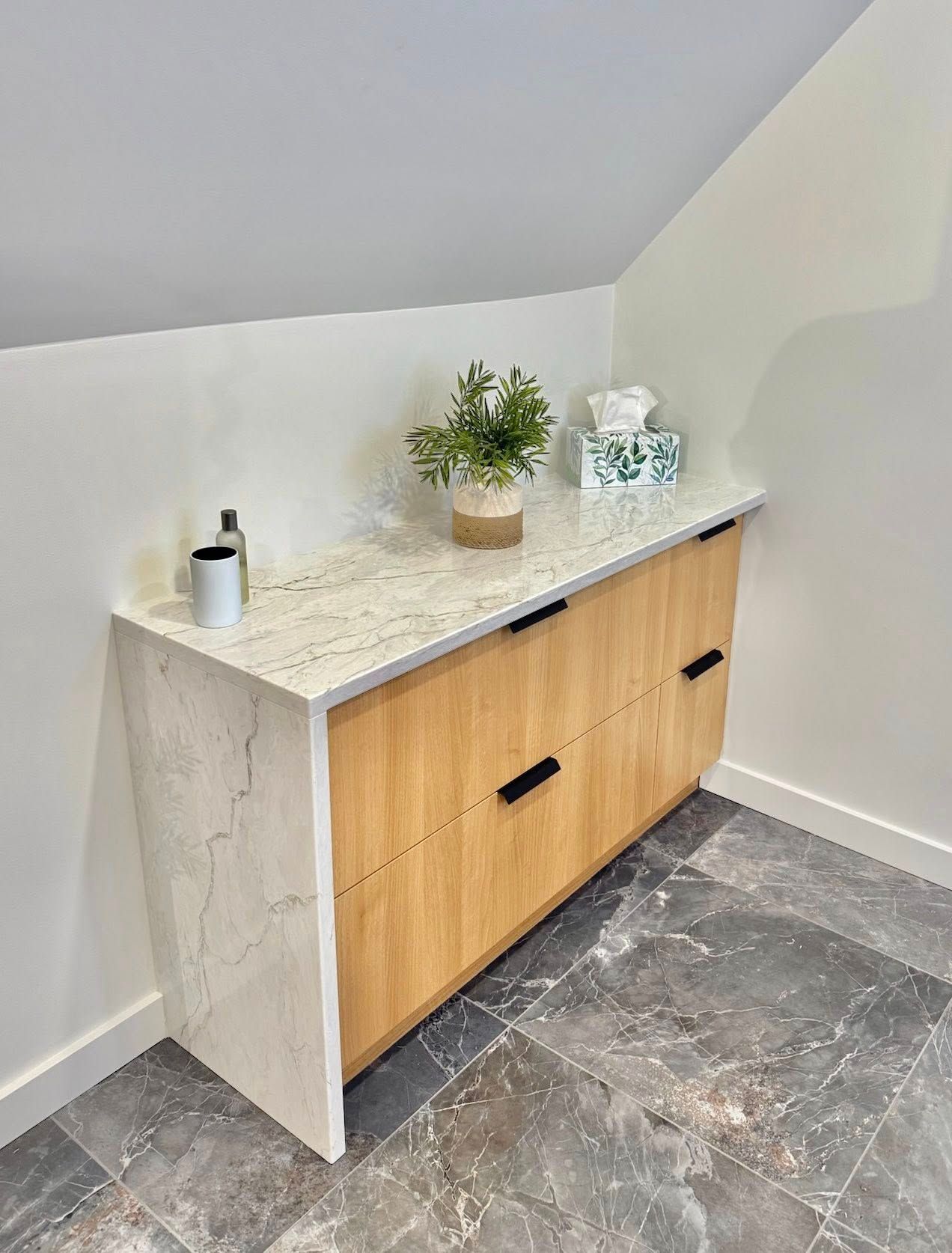 Meuble intégré avec tiroirs en bois clair, comptoir en pierre blanche et objets décoratifs dans une pièce en angle.