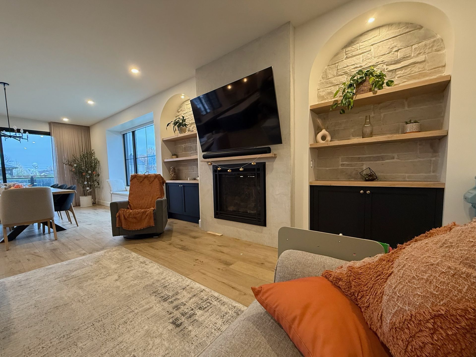 Salon avec cheminée, étagères cintrées, grande télévision et coin salon. Parquet clair et couleurs neutres.