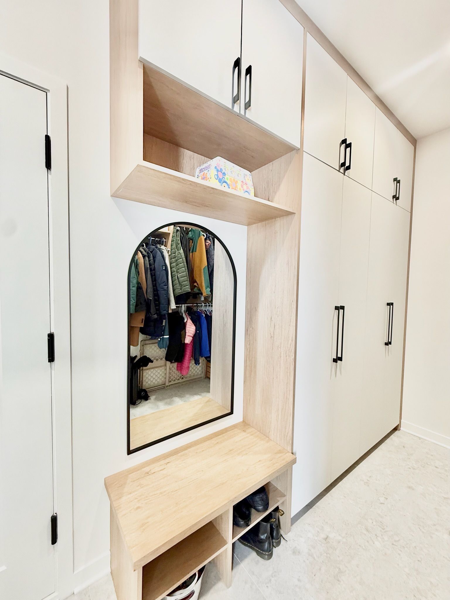 Meuble d'entrée intégré avec banc, miroir, étagères et placards. Finition bois clair et blanc.