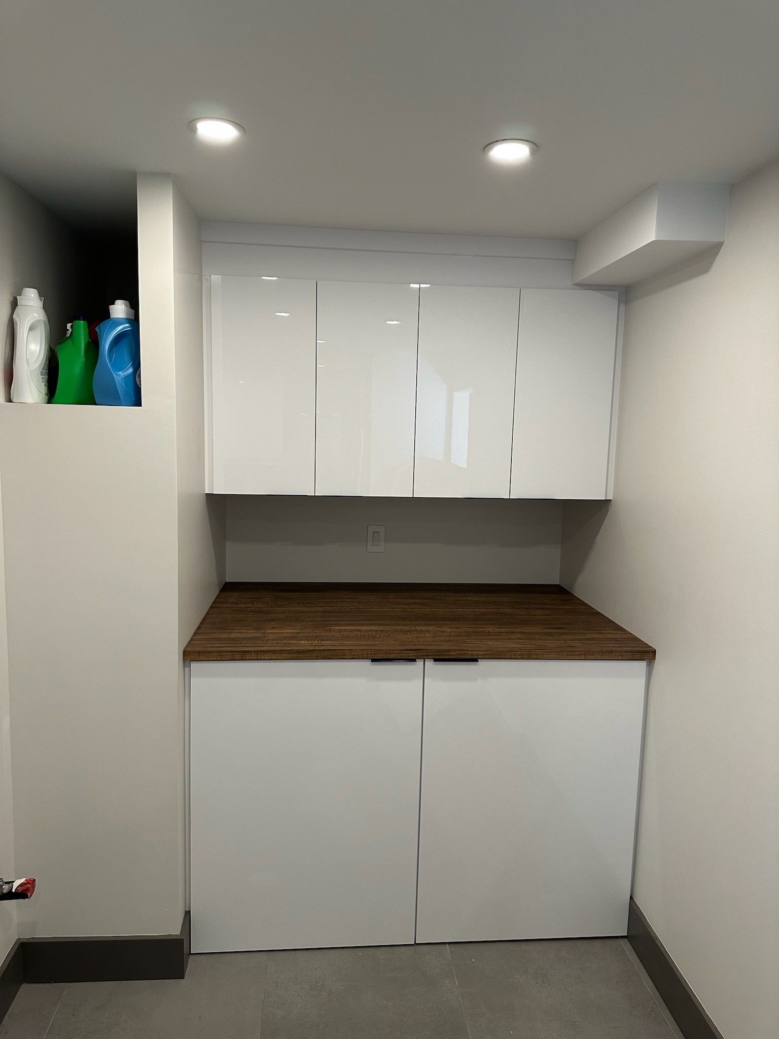 Buanderie avec placards blancs, plan de travail en bois foncé et niche pour la lessive.