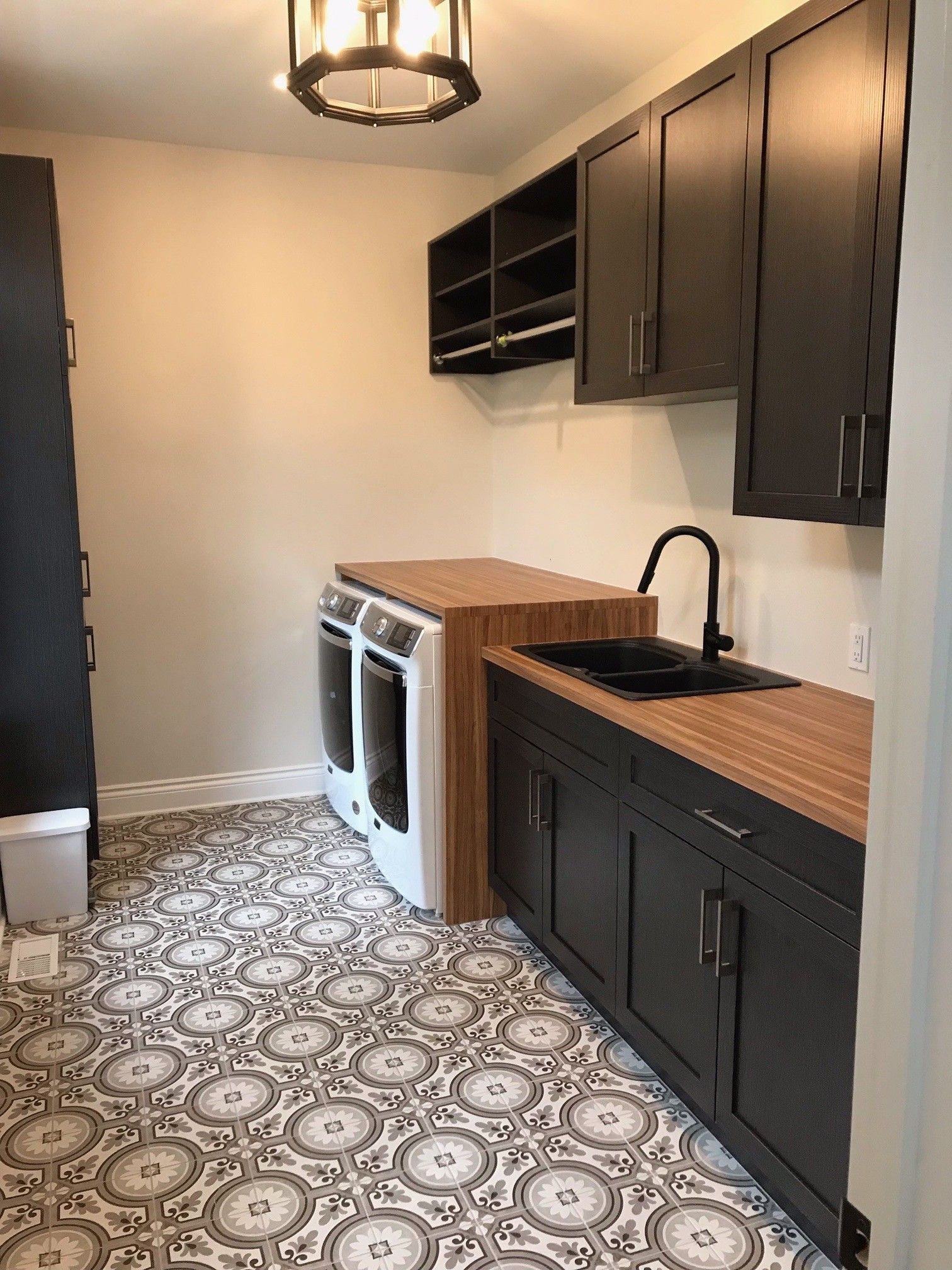 Buanderie avec placards noirs, plan de travail en bois massif, sol à motifs et appareils électroménagers blancs.