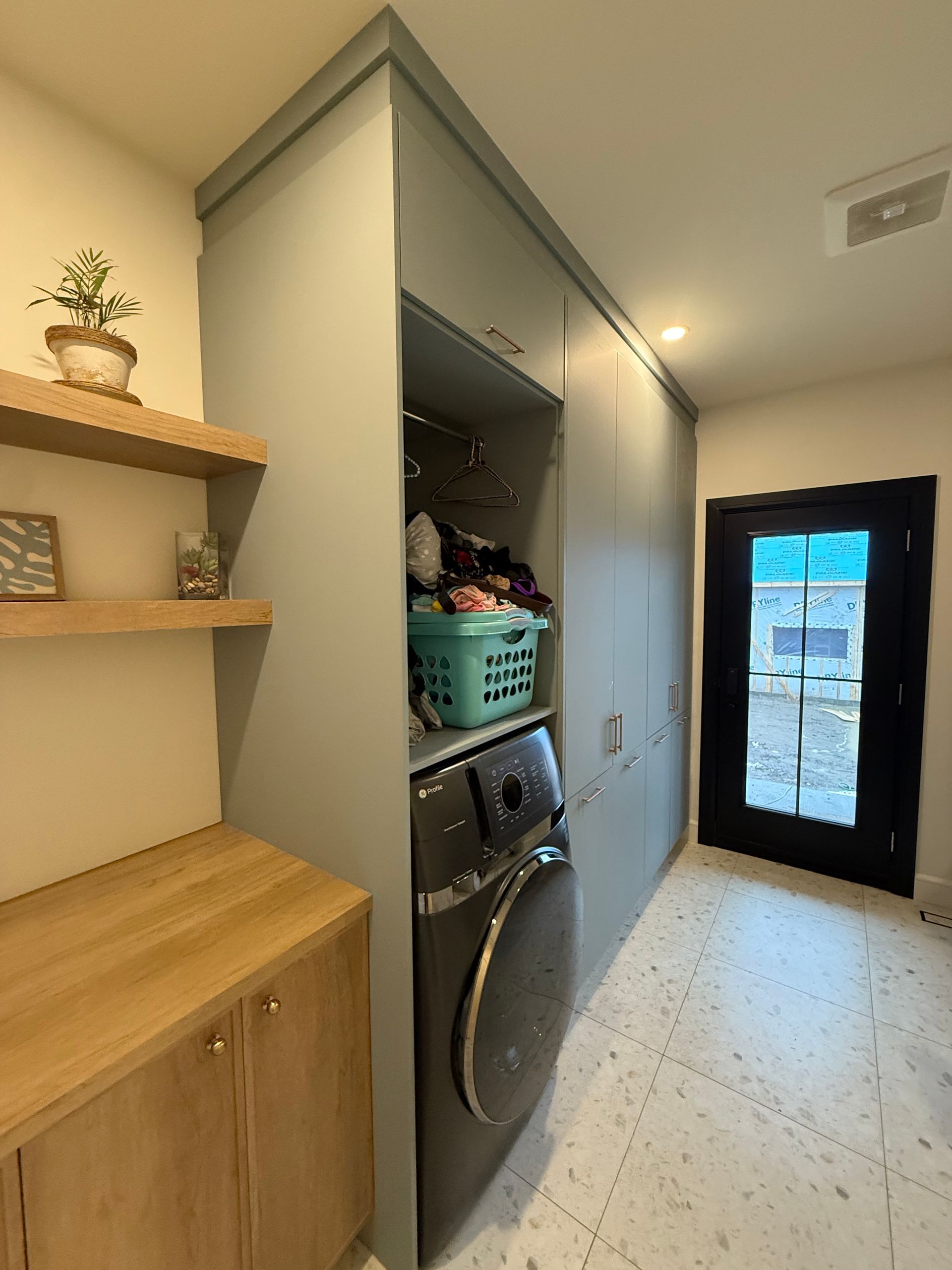 Buanderie avec placards bleus, machine à laver, plan de travail en bois et porte ouverte.