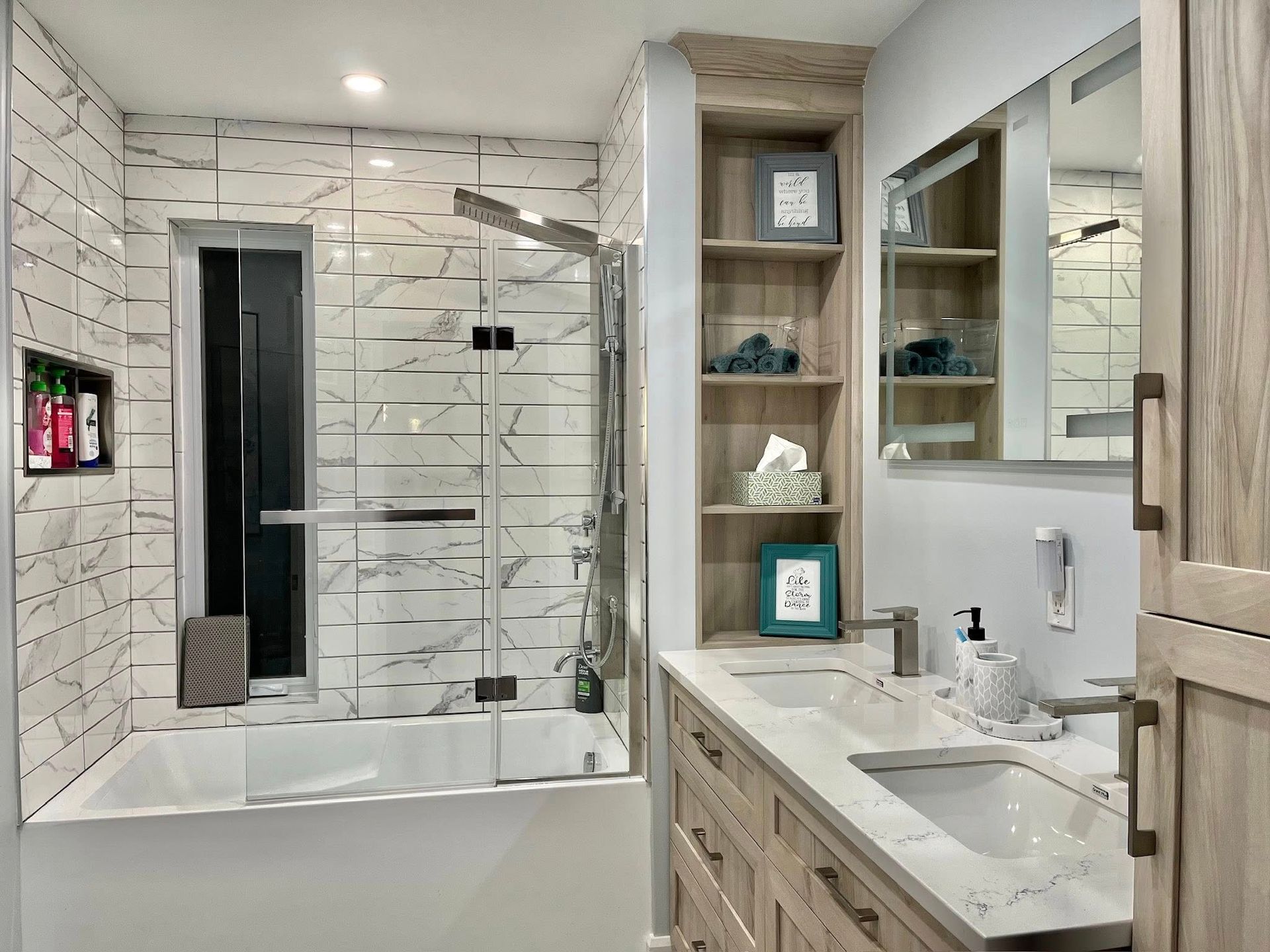 Salle de bains moderne avec carrelage en marbre, douche en verre, meubles en bois clair et étagères intégrées.