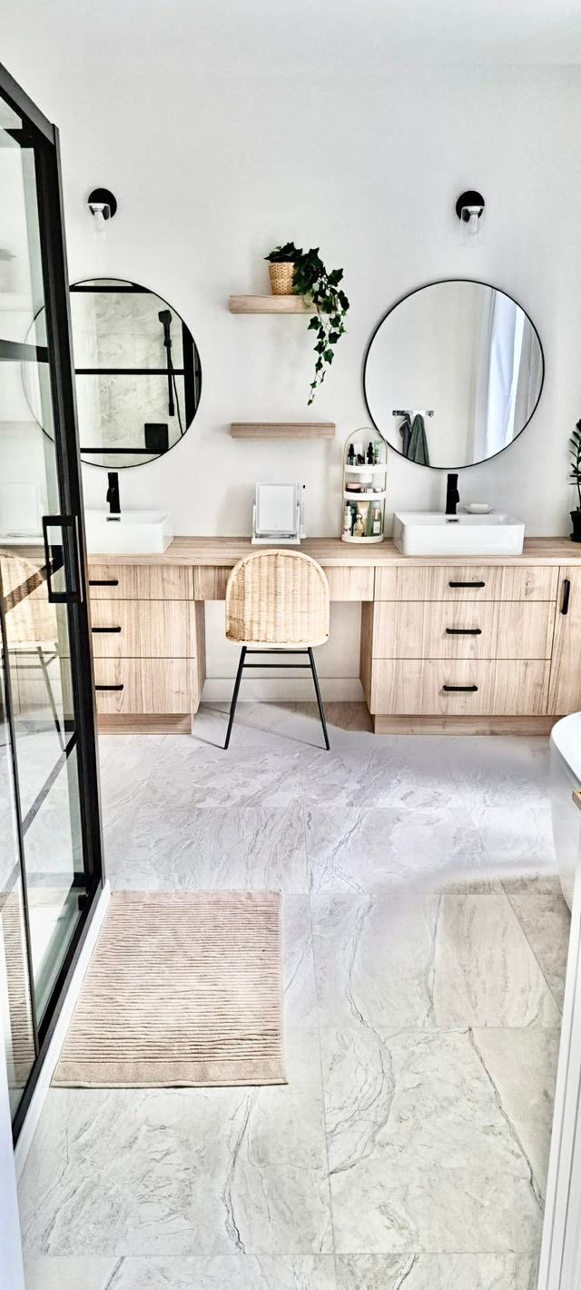 Une salle de bains moderne avec des meubles en bois clair, des miroirs ronds et une chaise de coiffeuse.