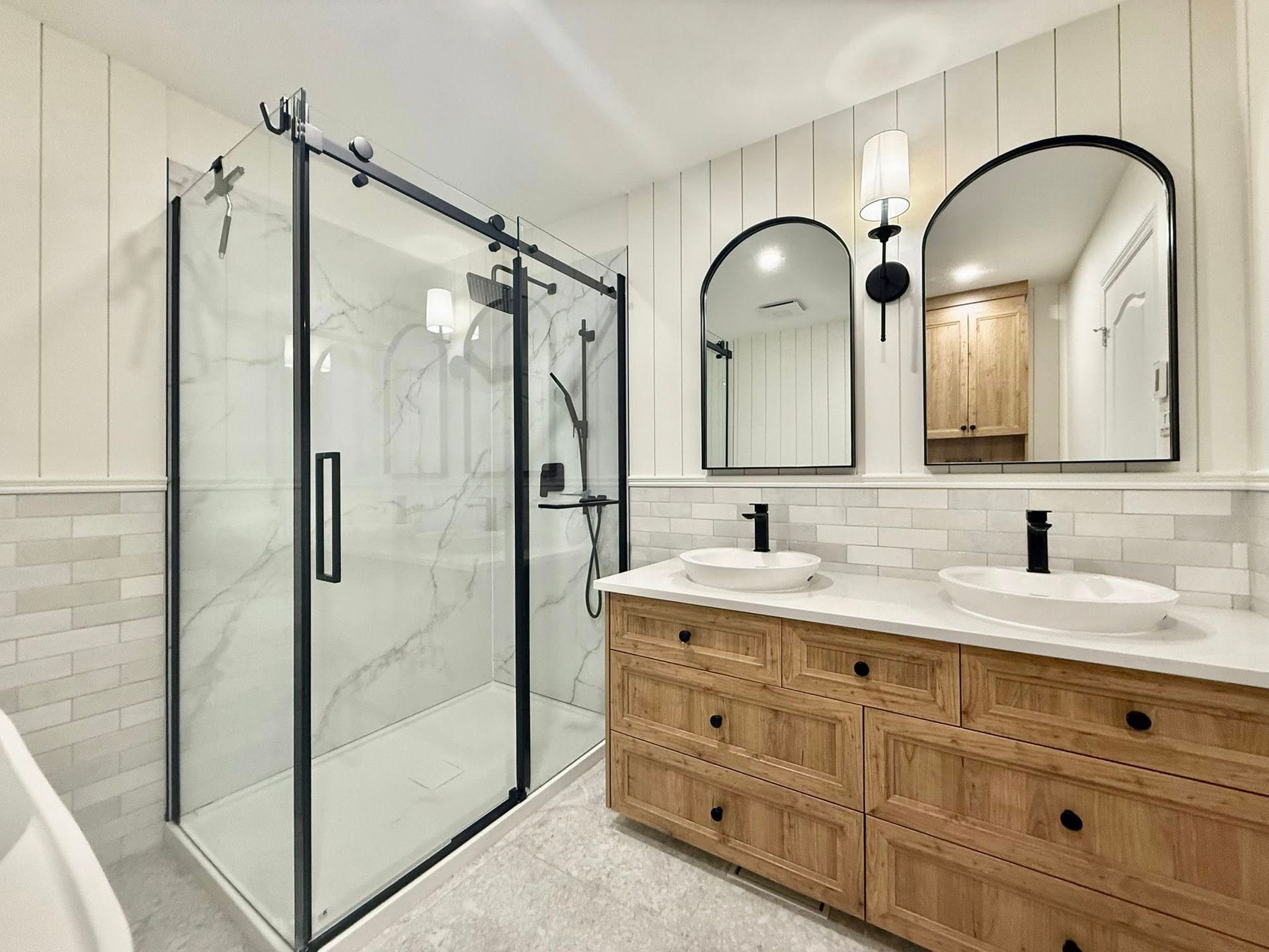 Salle de bains avec douche en verre, meuble-lavabo en bois et miroirs arqués.