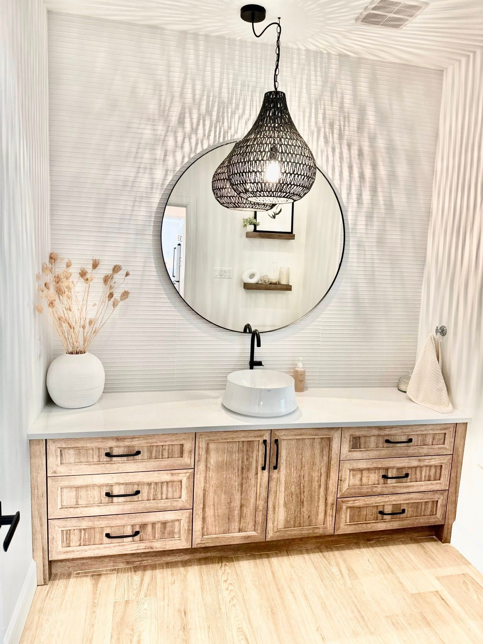 Salle de bains avec meuble-lavabo en bois, miroir rond et suspension lumineuse en osier.