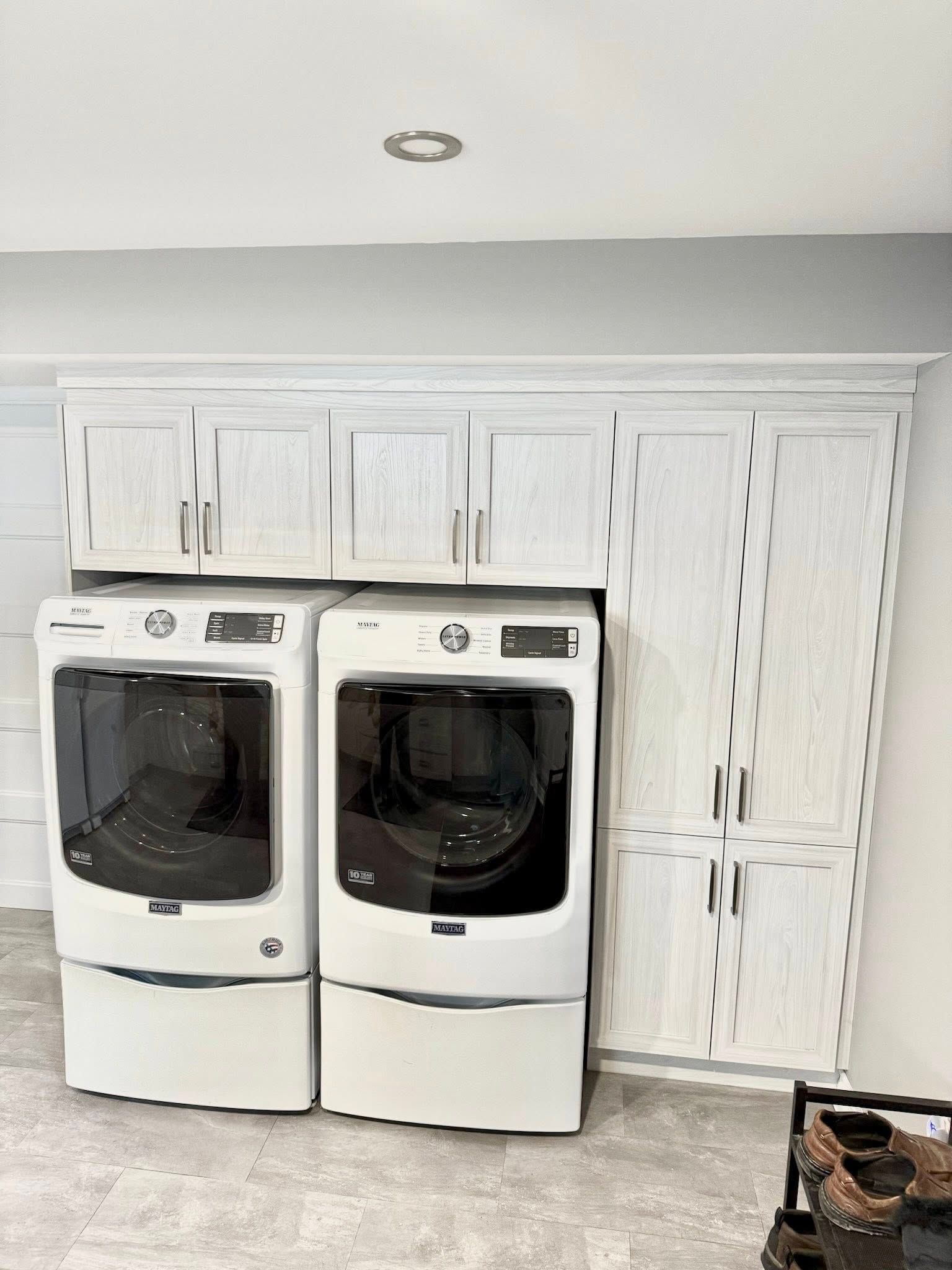 Laveuse et sécheuse blanches avec armoires suspendues et armoire haute dans une buanderie.