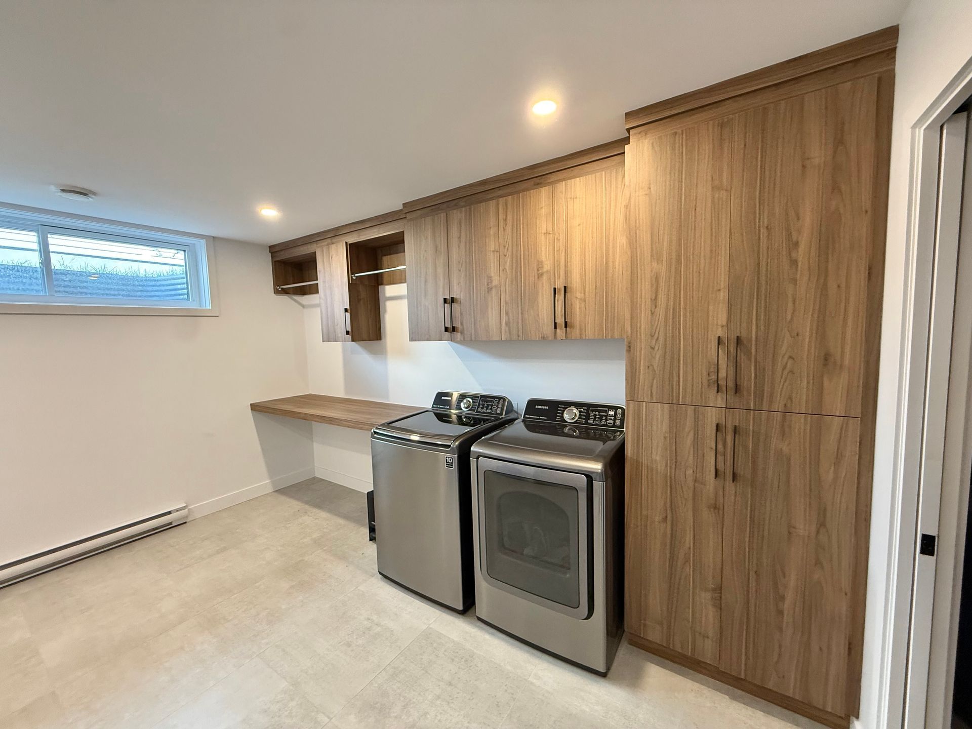 Buanderie avec placards en bois, lave-linge, sèche-linge et bureau intégré.