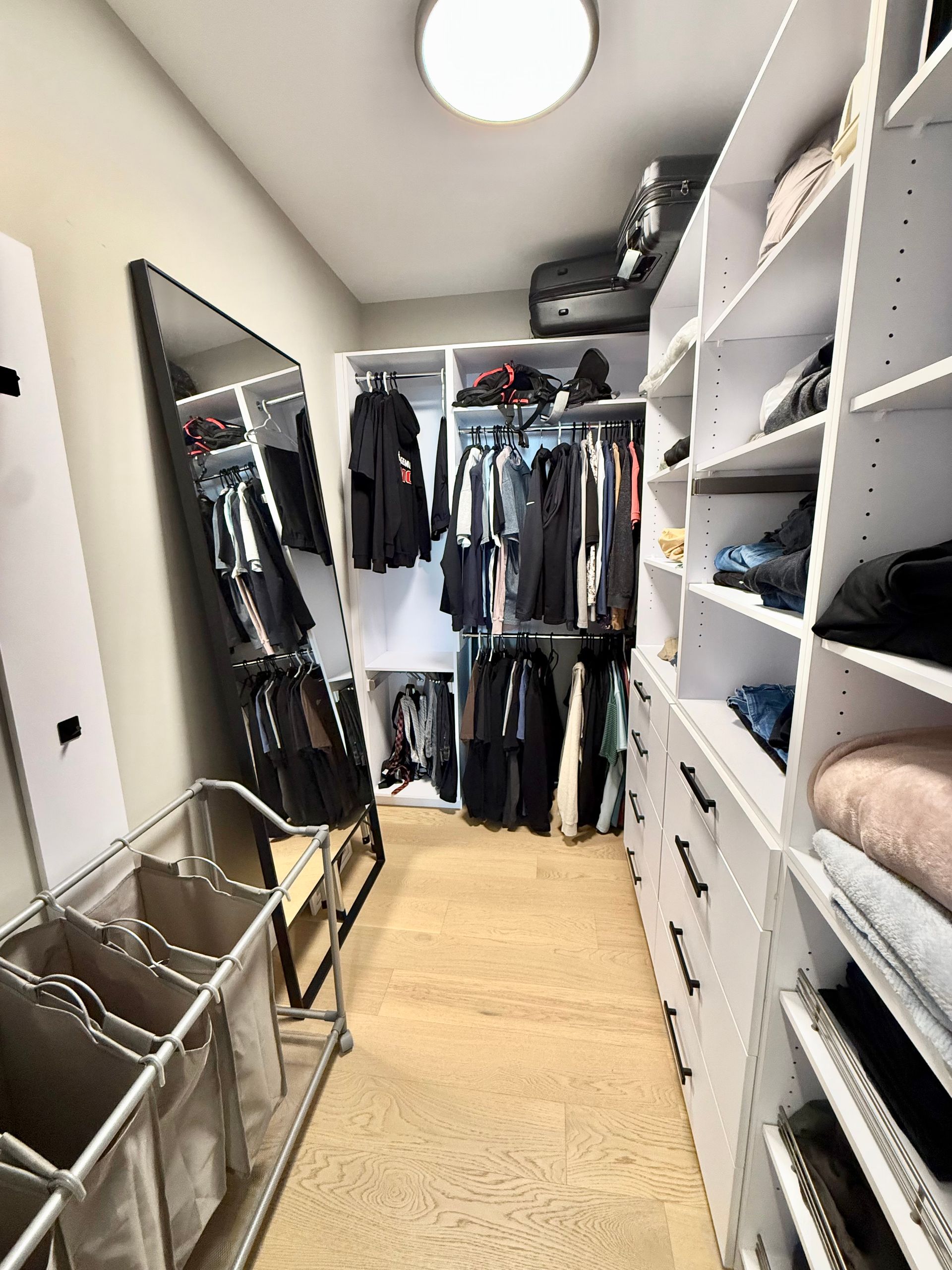 Dressing avec étagères blanches, vêtements, miroir en pied et trieur à linge.