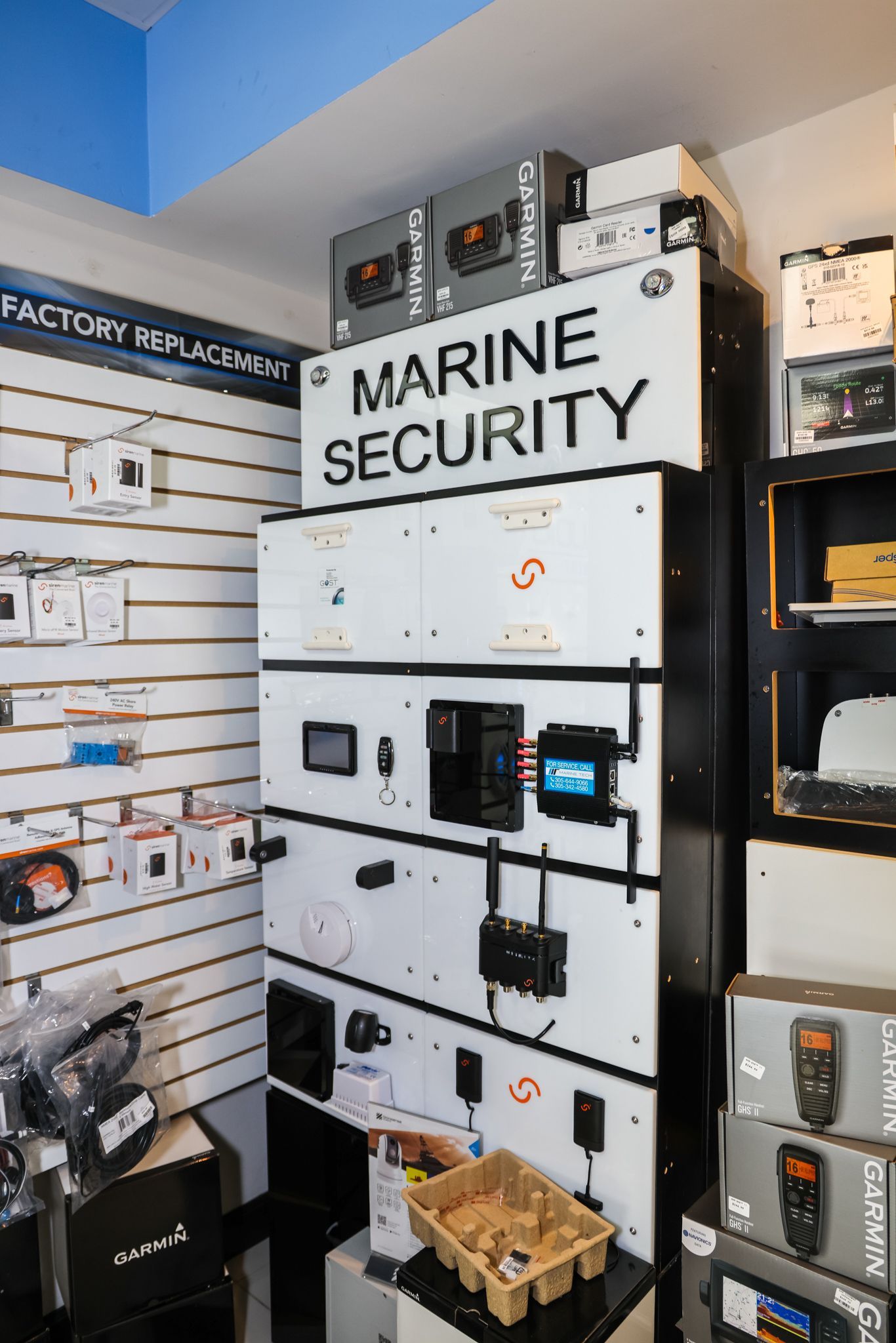 Marine security system display in a store. White cabinet with electronic devices, signage, and product boxes.