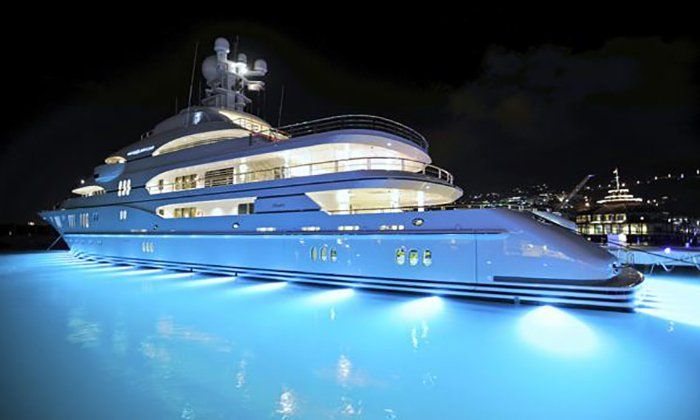 Luxury yacht illuminated with blue lights at night in a harbor.