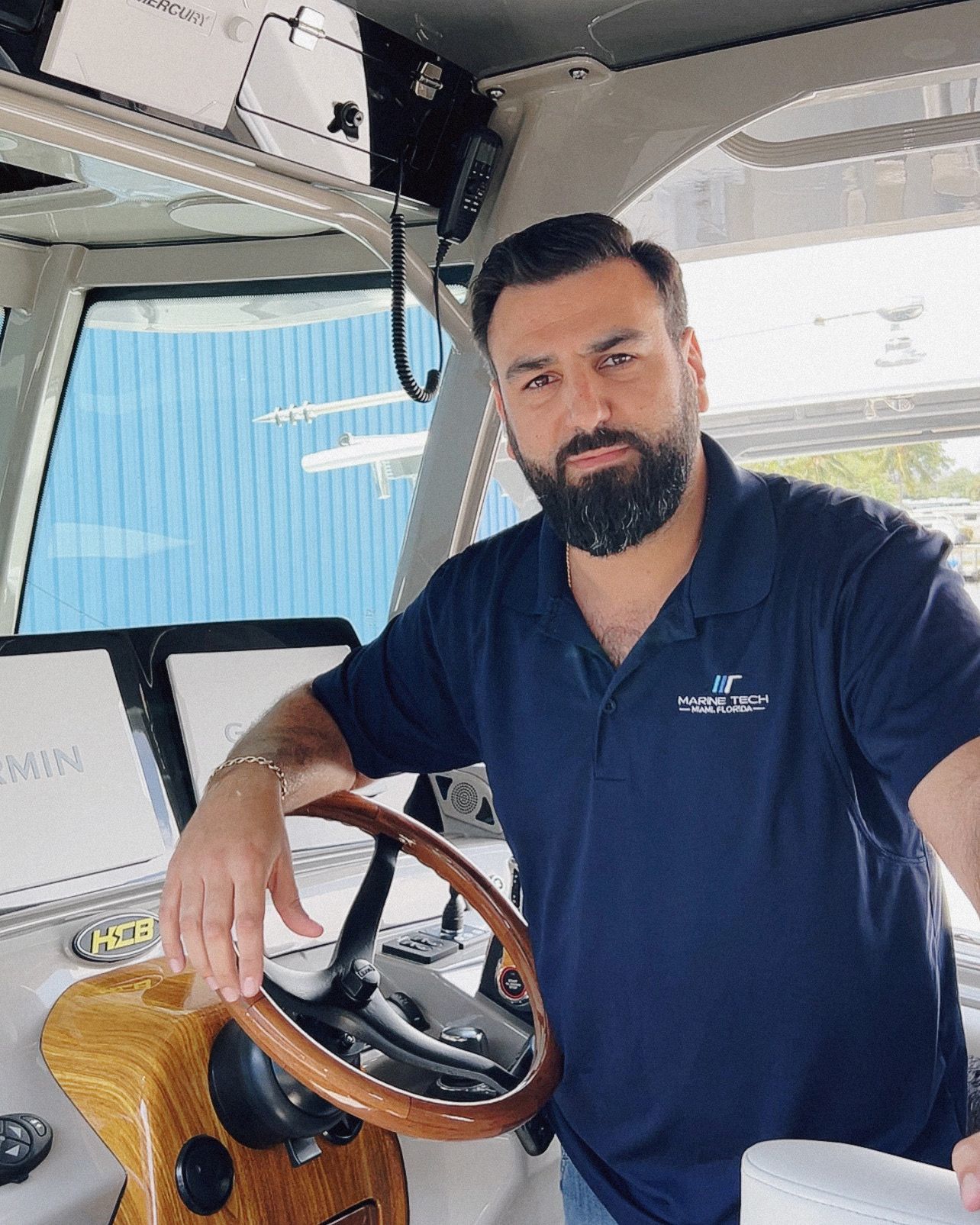 A man with a beard is standing in the cockpit of a boat.