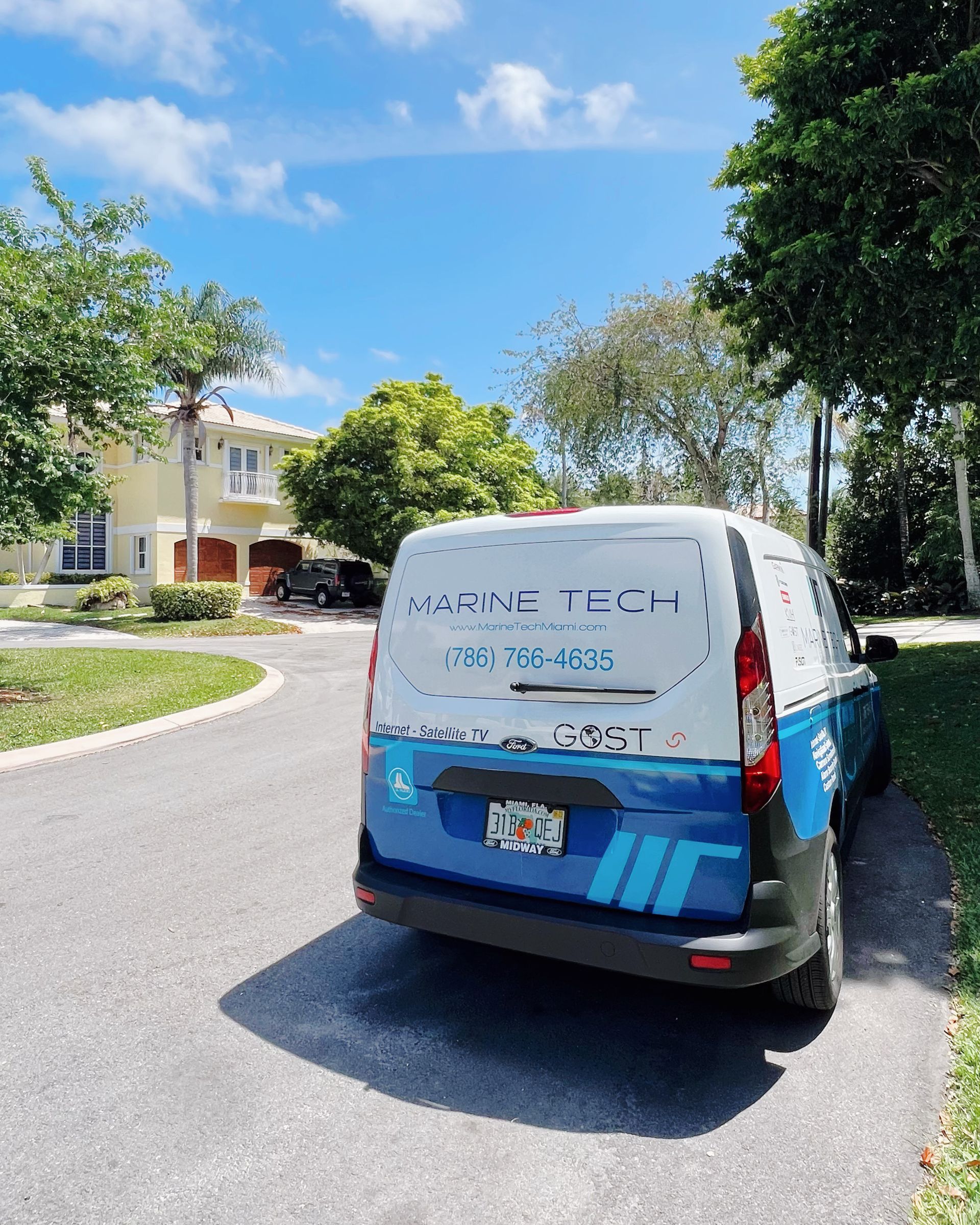 A blue and white van is parked on the side of the road in front of a house.