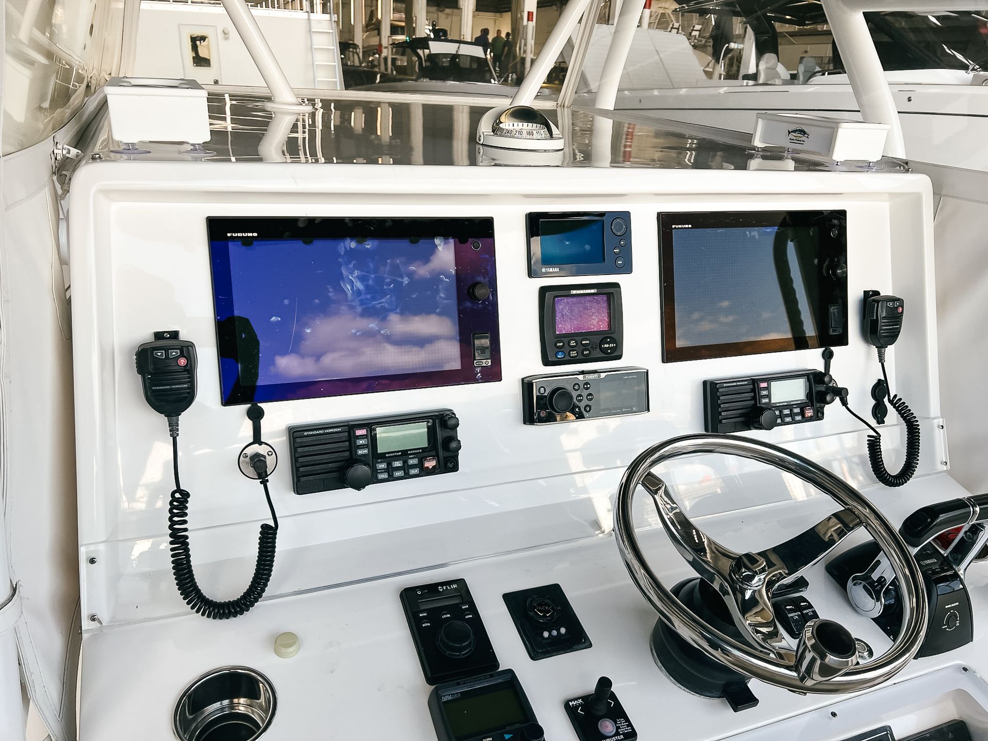 A steering wheel and dashboard of a boat with a lot of electronics on it.
