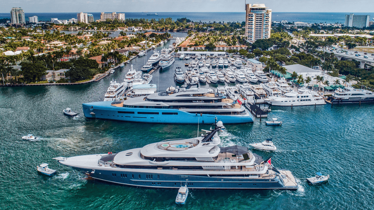 Aerial view of yachts docked at a harbor, with a light blue and dark blue boat in the foreground.