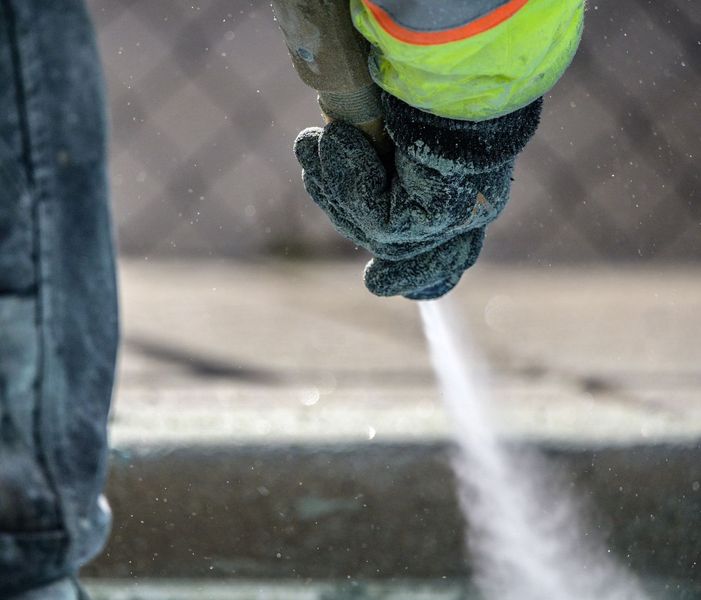 A person wearing gloves is spraying water from a hose.
