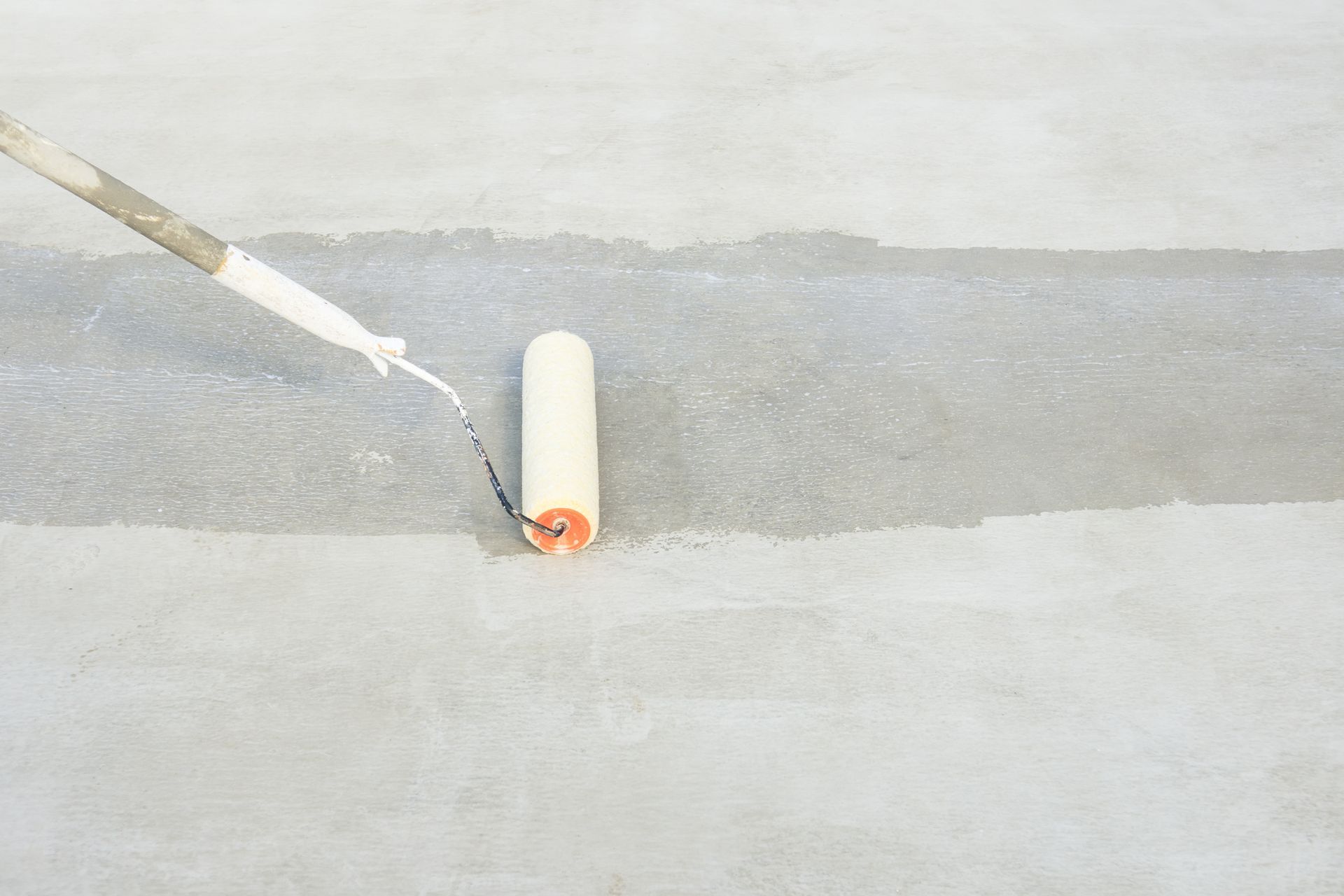 A person is painting a concrete floor with a paint roller.