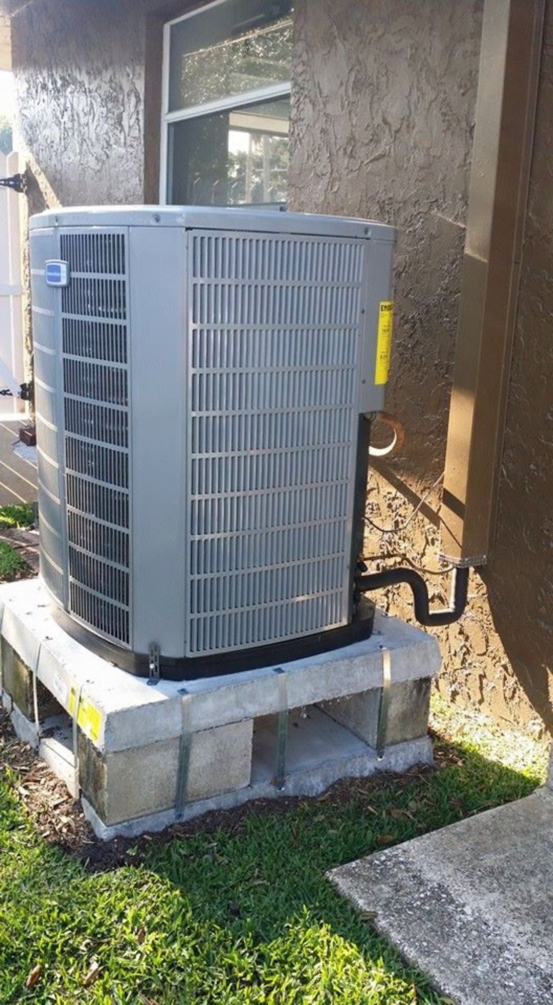 A large air conditioner is sitting on top of a concrete block next to a house.