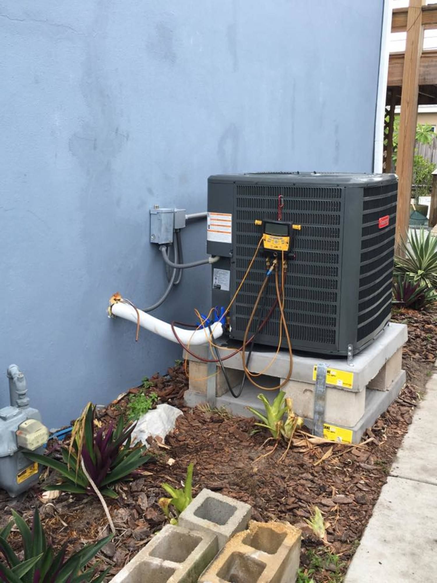 An air conditioner is sitting on top of a concrete block next to a sidewalk.