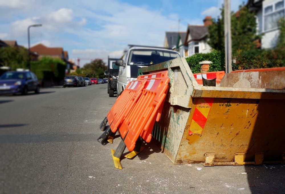 A Dumpster Is Sitting on The Side of The Road Next to A Row of Orange Barriers — Barry's Recycling in Brisbane, QLD