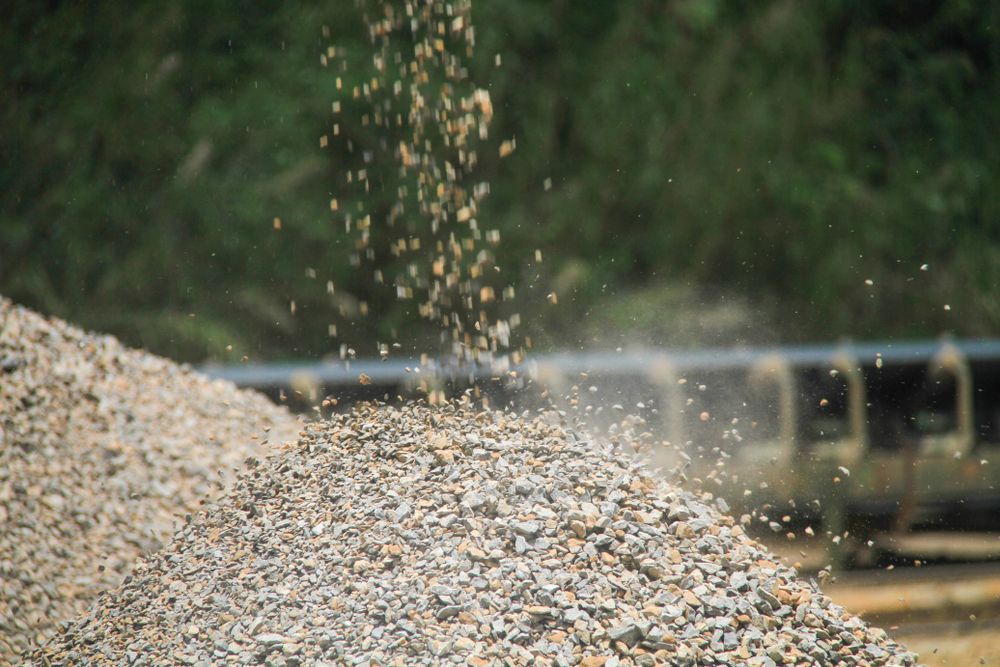 Gravel Being Poured Onto a Large Pile and Green Hillside in Background.