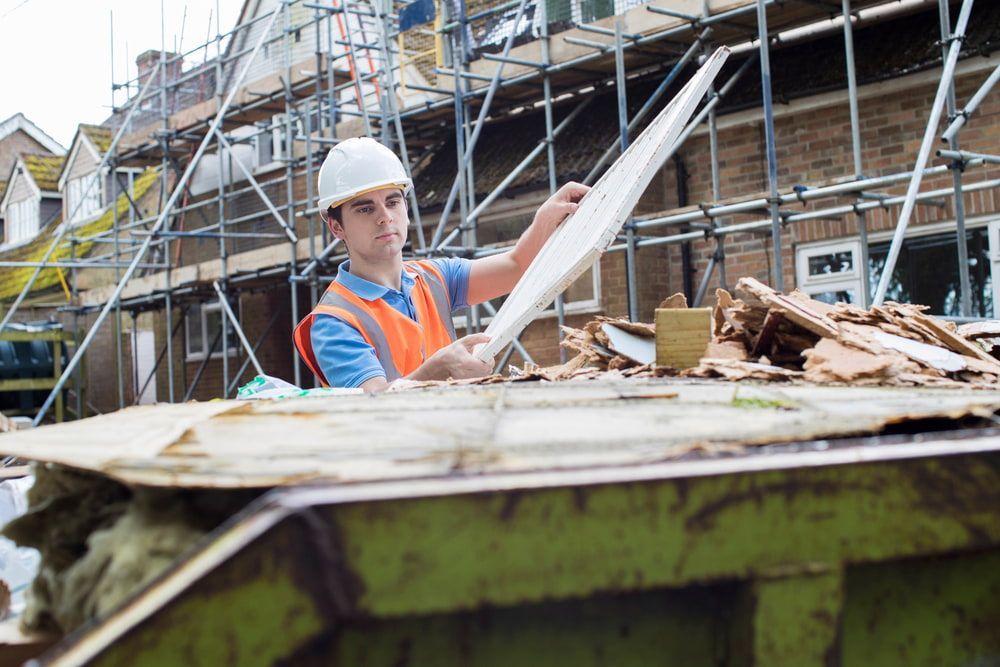 Construction worker in hard hat sorting debris from a dumpster at a busy construction site.
