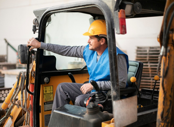Man in a hard hat and blue vest operating construction equipment.