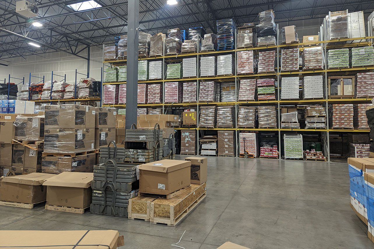 Warehouse interior with pallets stacked high on shelves, containing various packaged goods.