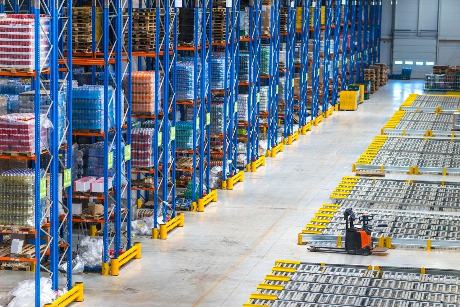 Warehouse interior with tall blue shelving units stocked with goods and an orange forklift.