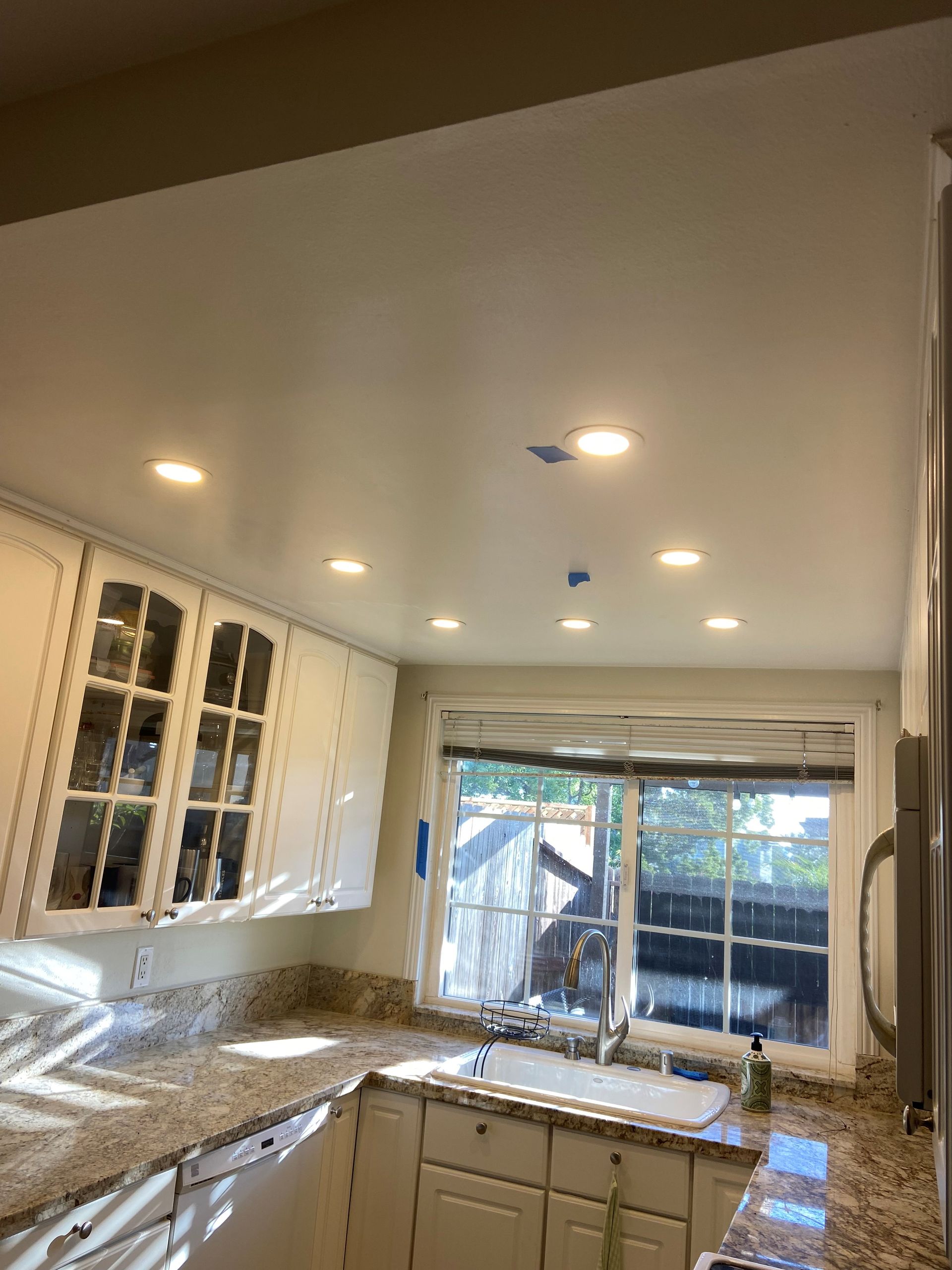 A kitchen with white cabinets , granite counter tops , a sink and a window.