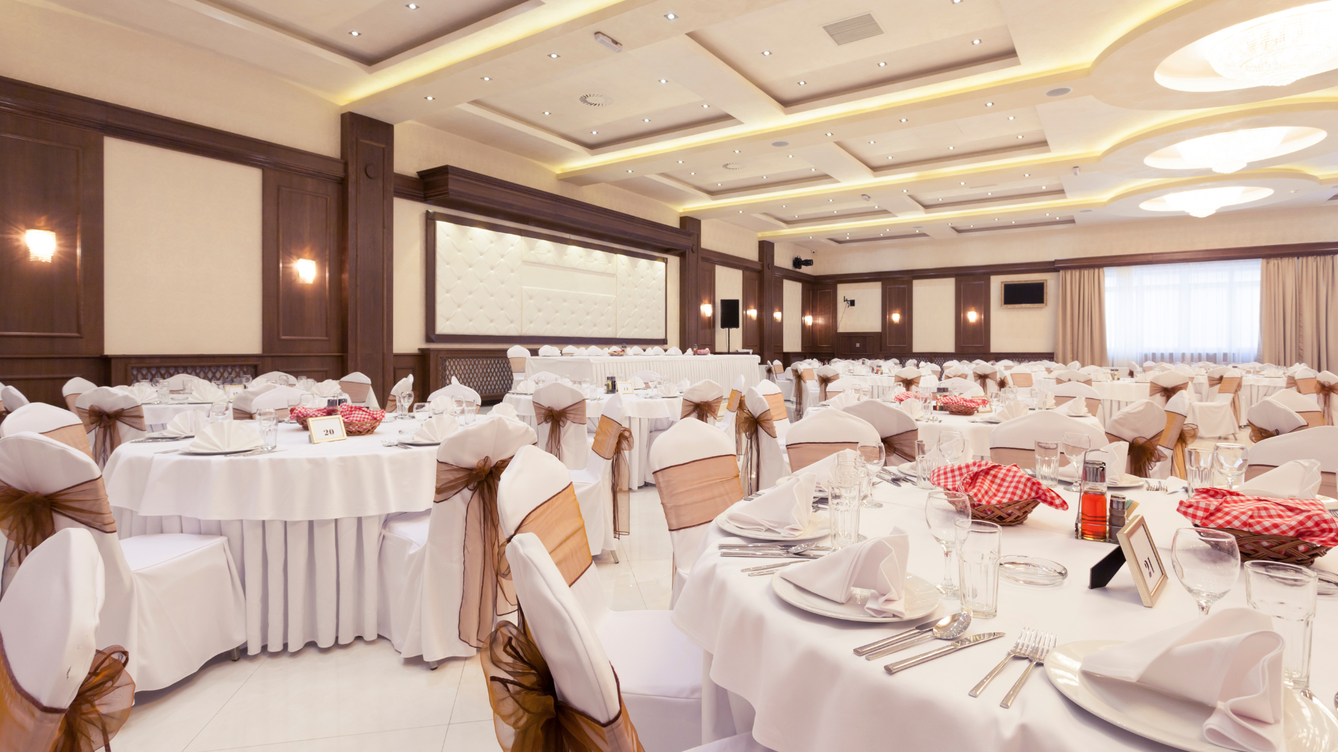 Banquet hall with tables set for a formal event, featuring white linens and decorative chair covers.