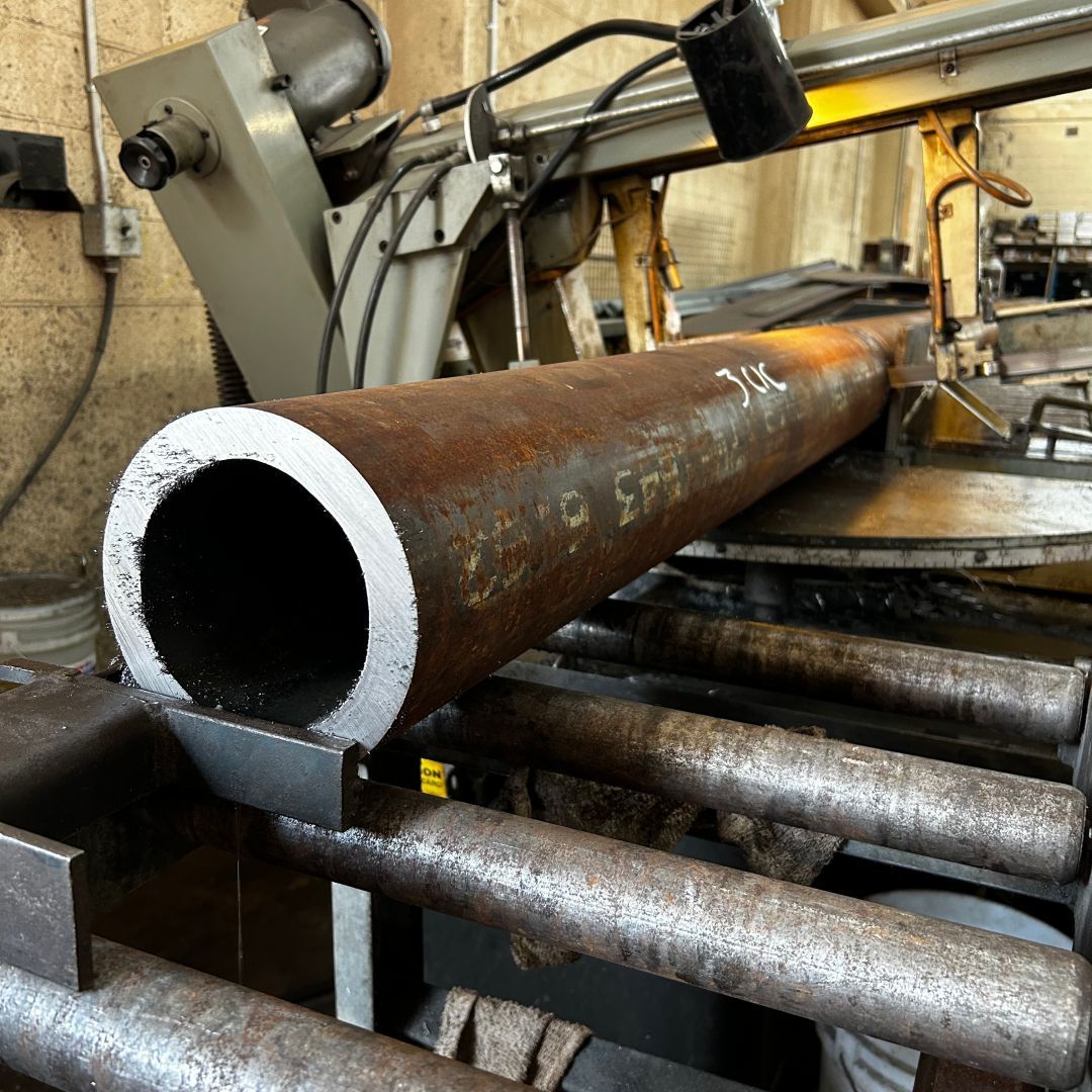 A large metal pipe is being cut by a machine