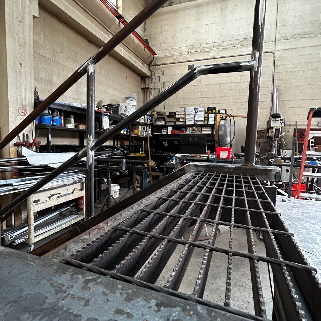 A metal staircase in a factory with a ladder in the background