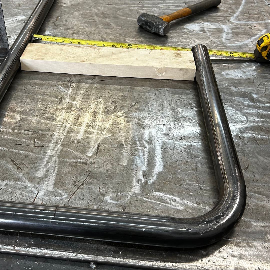 A metal pipe is sitting on a table next to a hammer and a tape measure.