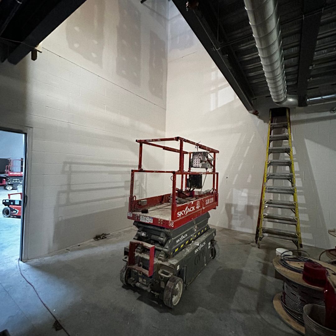 A red scissor lift in a room with a ladder