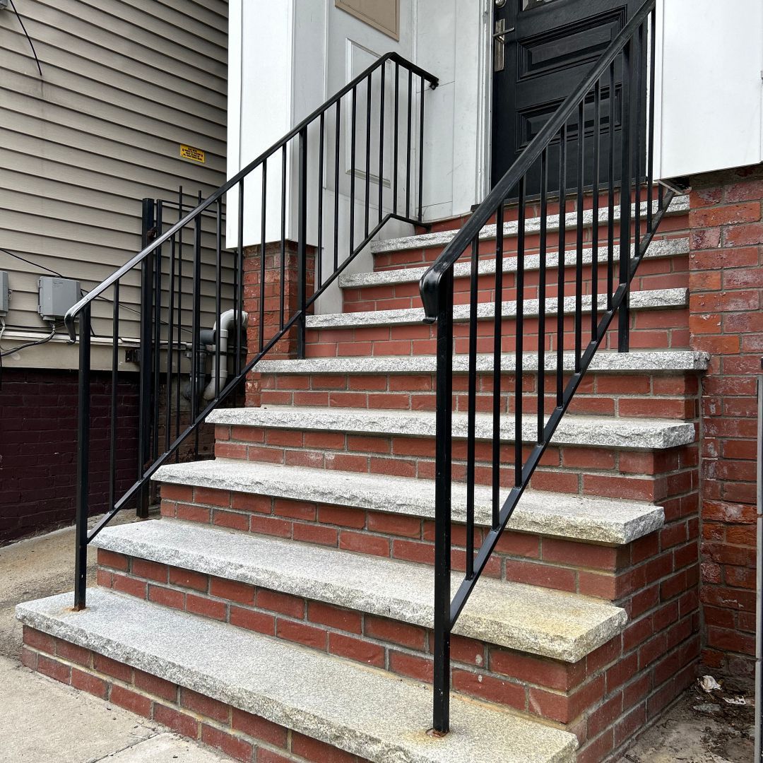 A set of stairs with a black railing and a brick wall.