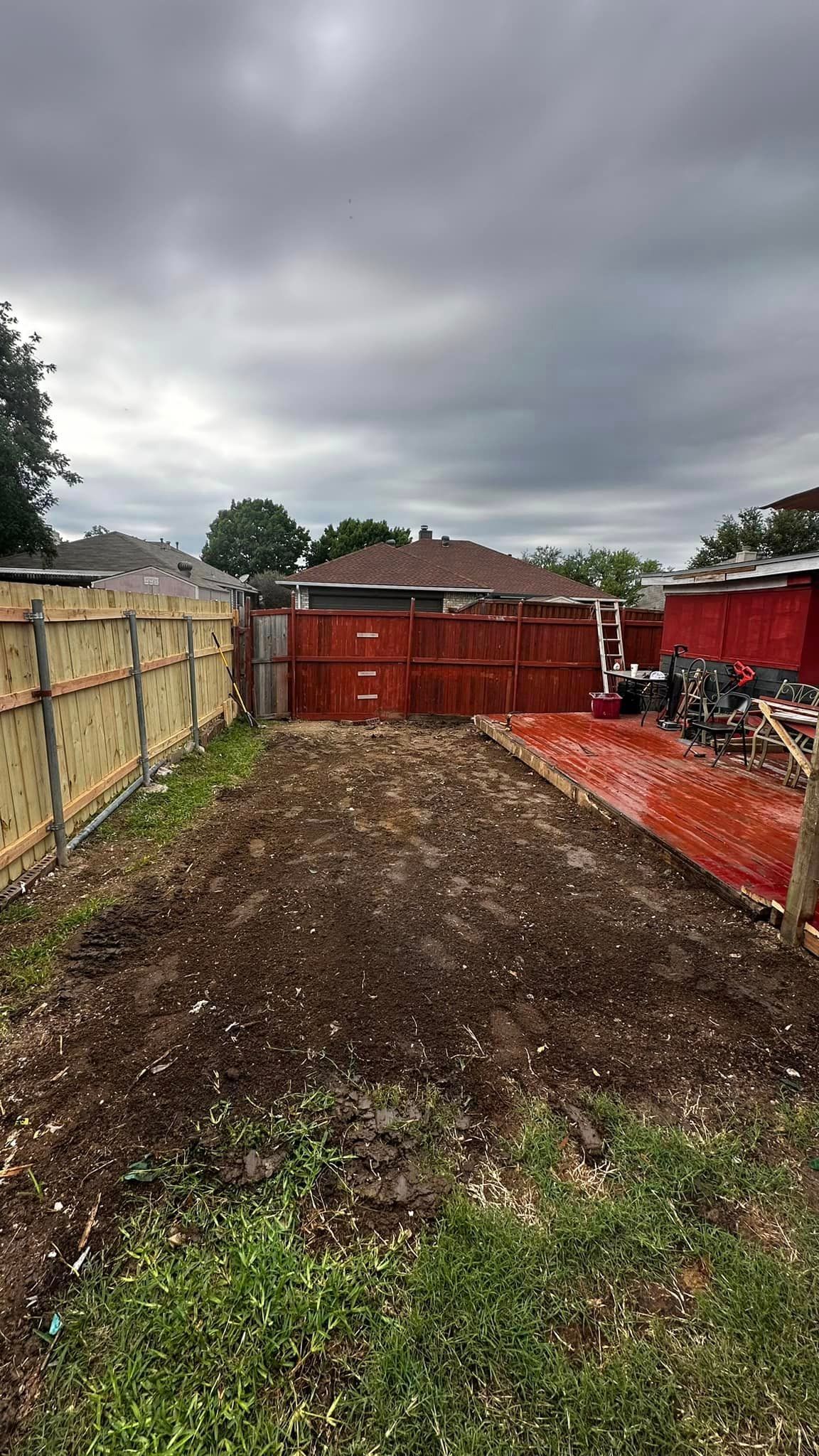 A dirt yard with a red fence and a house in the background.