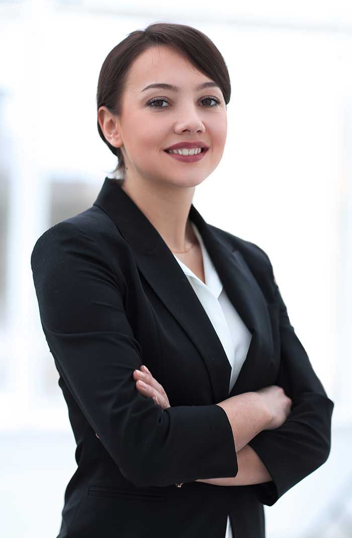 Woman in a black blazer with arms crossed, smiling confidently in an office setting.