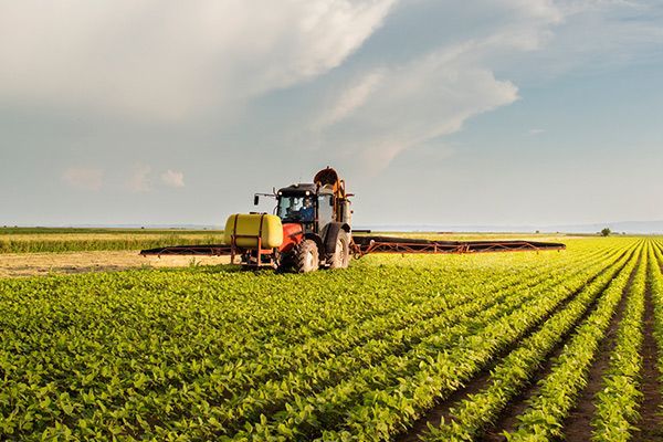 Tractor spraying crops in a field, under a partly cloudy sky.
