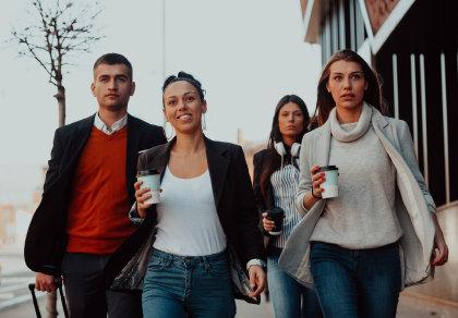 Four people walking, holding coffee cups, outside a brick building.