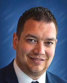 Man in suit smiling at the camera with a blue background.