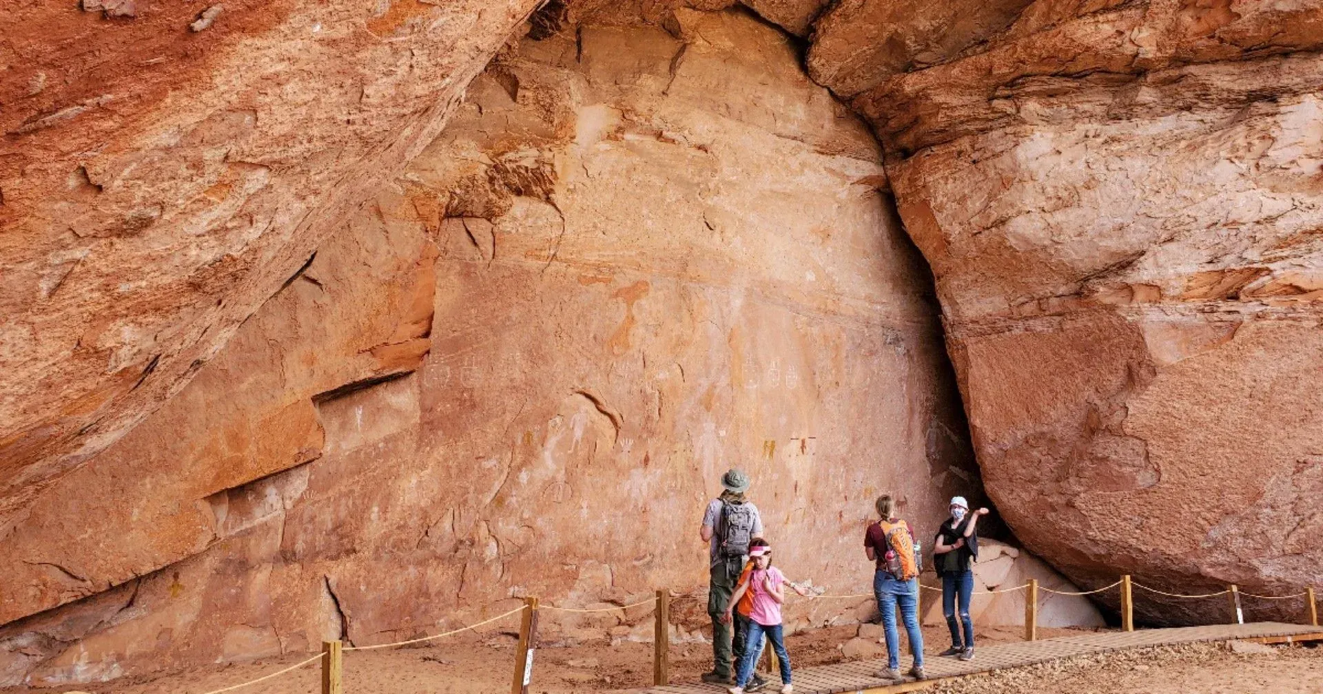 People standing inside a large red rock cave, looking up at the cliff wall.