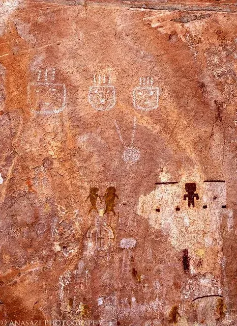 Ancient rock painting in red-brown stone with pale symbols and small human figures