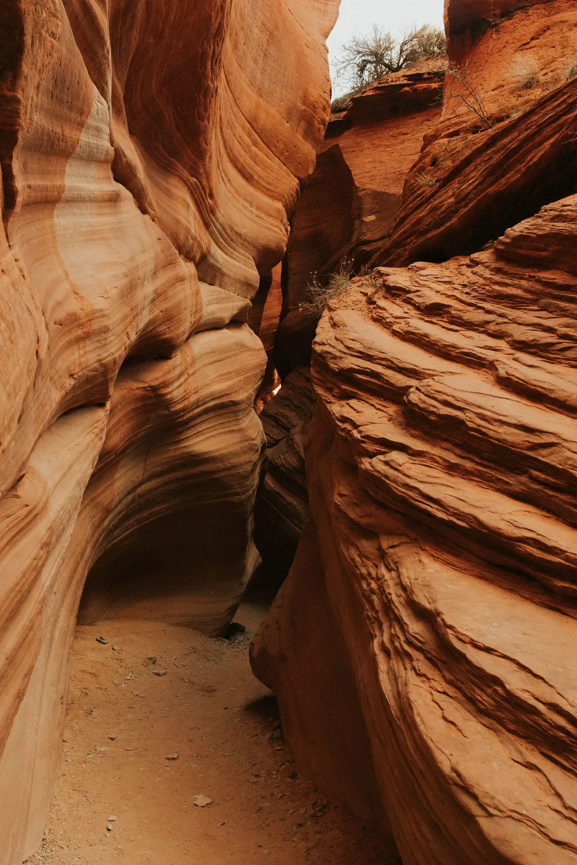 Narrow sandstone slot canyon with layered orange and red rock walls and sandy floor