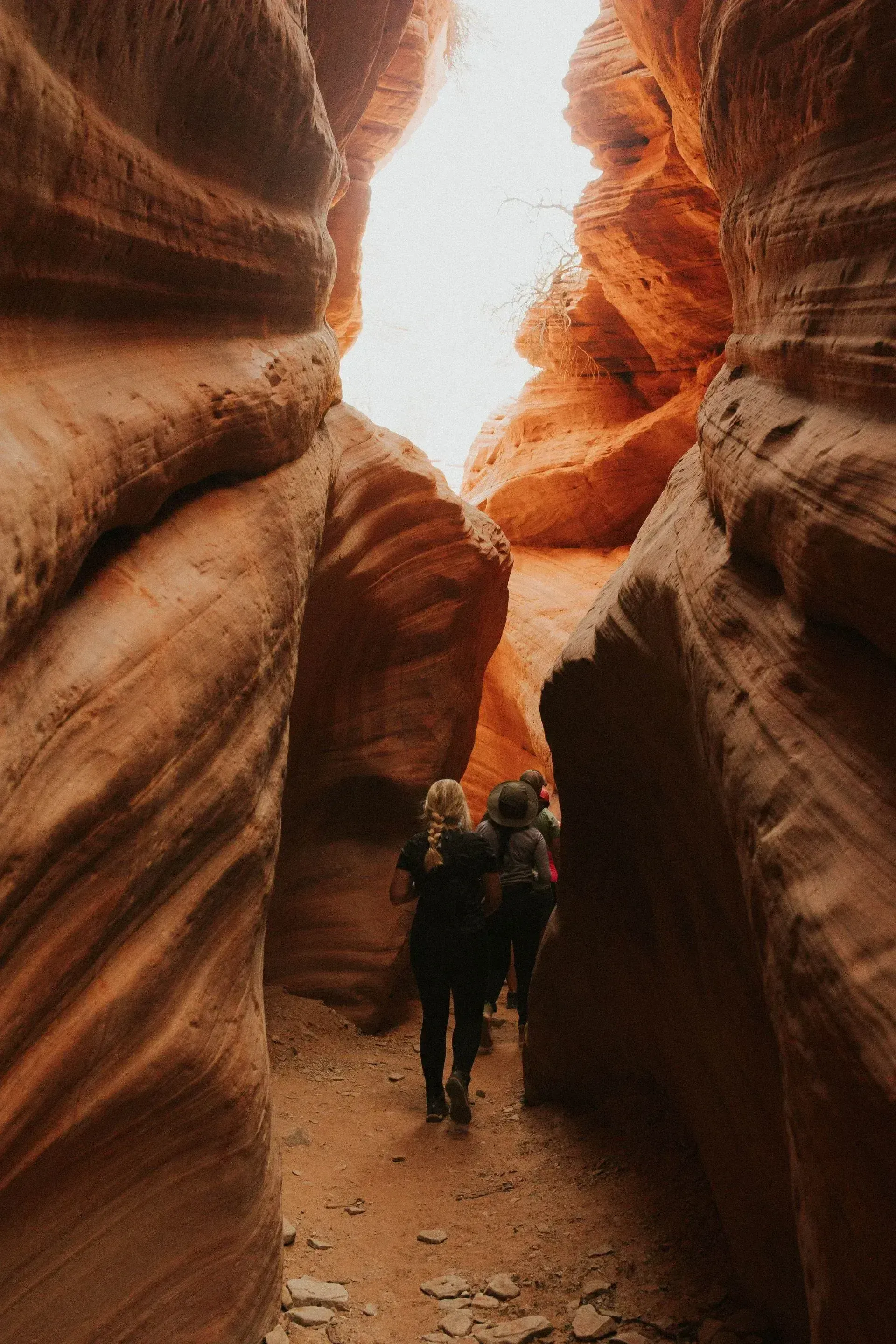 Two hikers walking through a narrow red sandstone canyon under bright light
