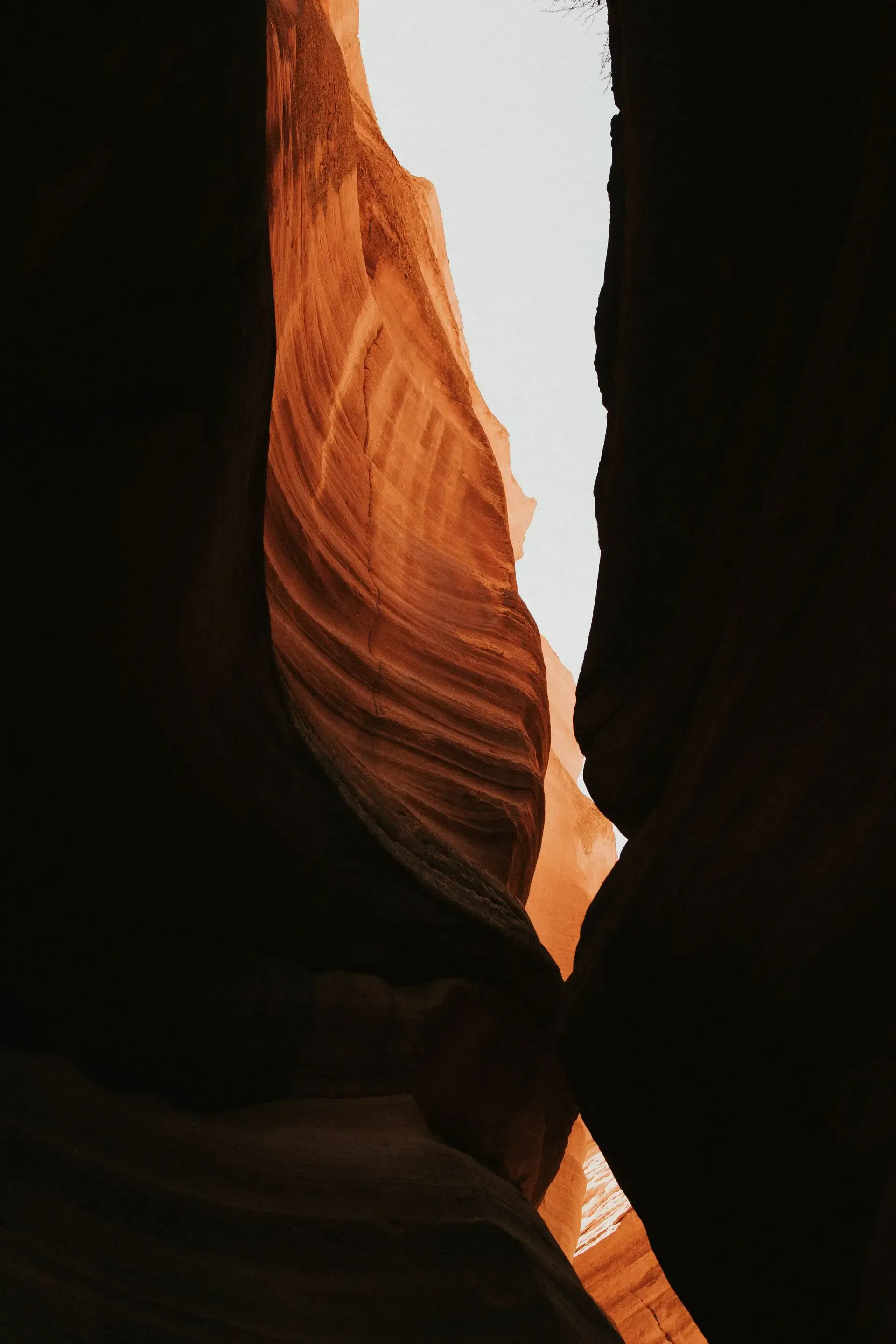 Narrow sunlit slot canyon with orange sandstone walls and a bright opening above